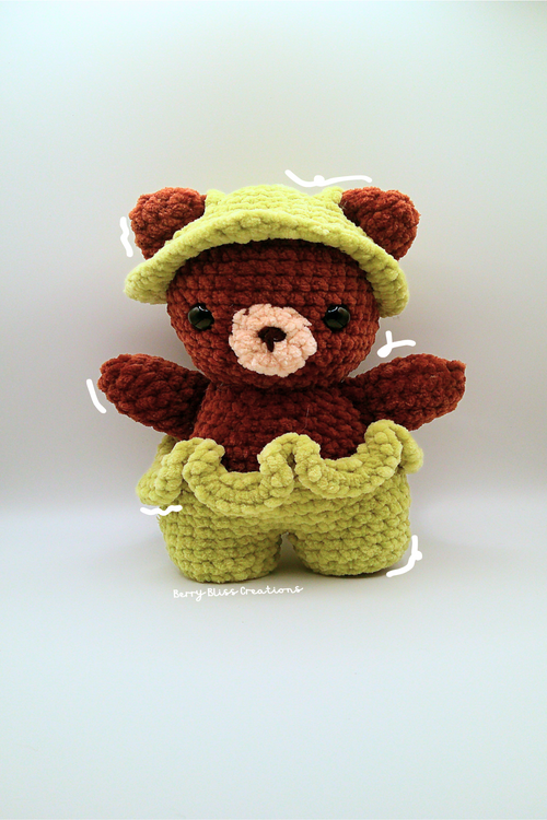 A crocheted teddy bear doll wearing a light green hat and matching pants.