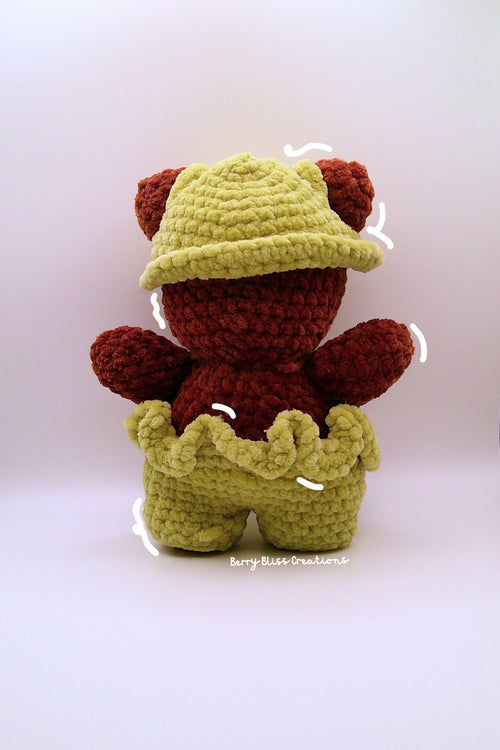 A handmade crocheted teddy bear doll wearing a yellow-green hat and matching pants.