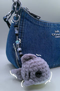 A small gray crocheted whale plush, (Coach bag not included)